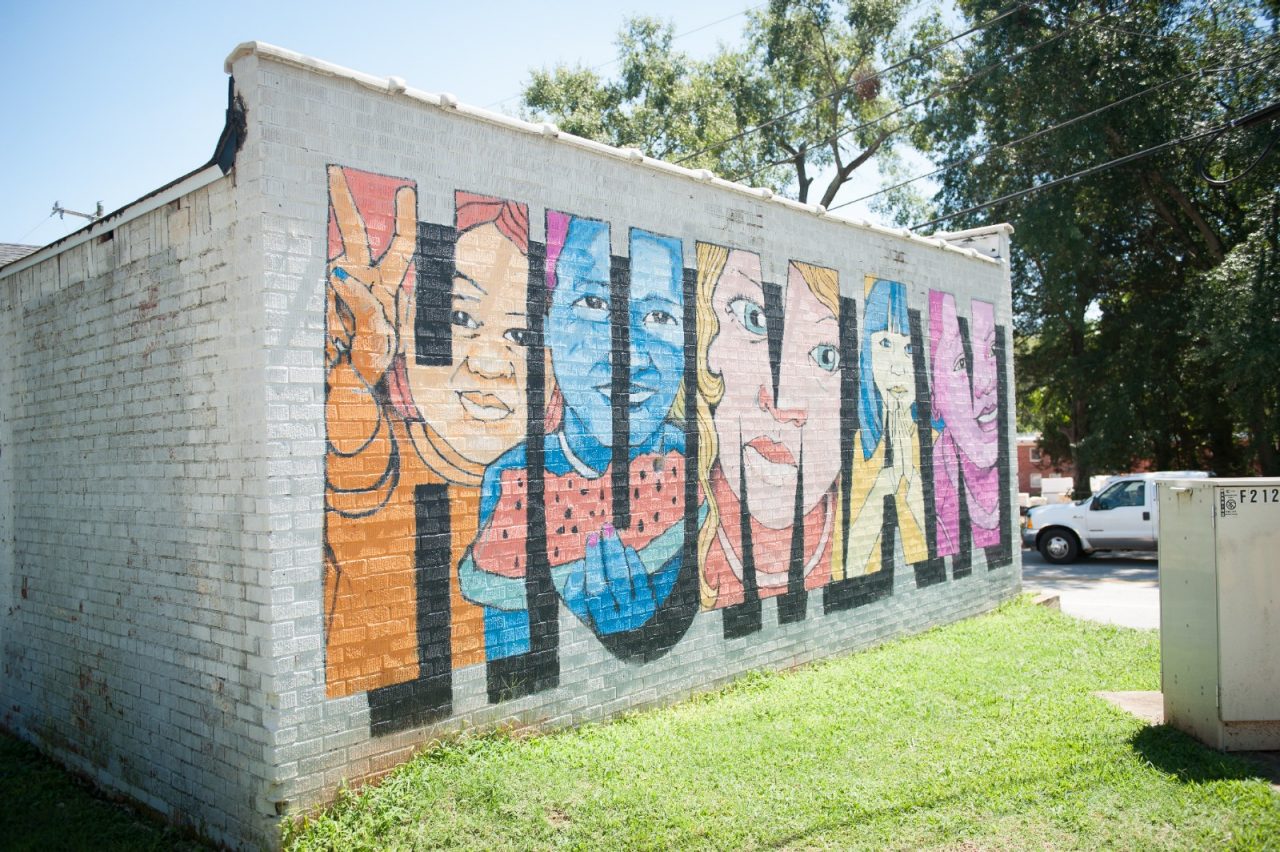 A mural, featuring children's faces, decorates a wall of a small brick building.