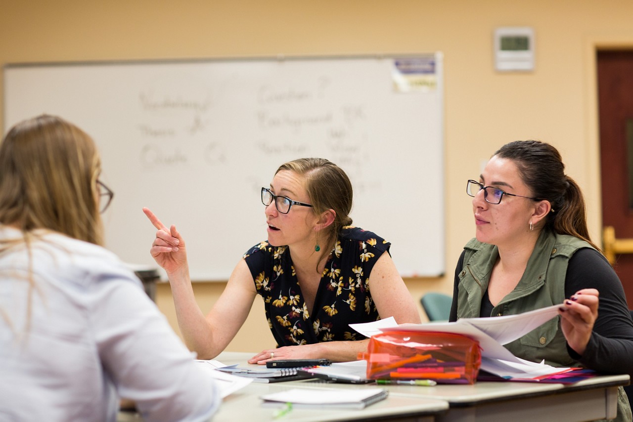 A teacher talking with two students wearing glasses.