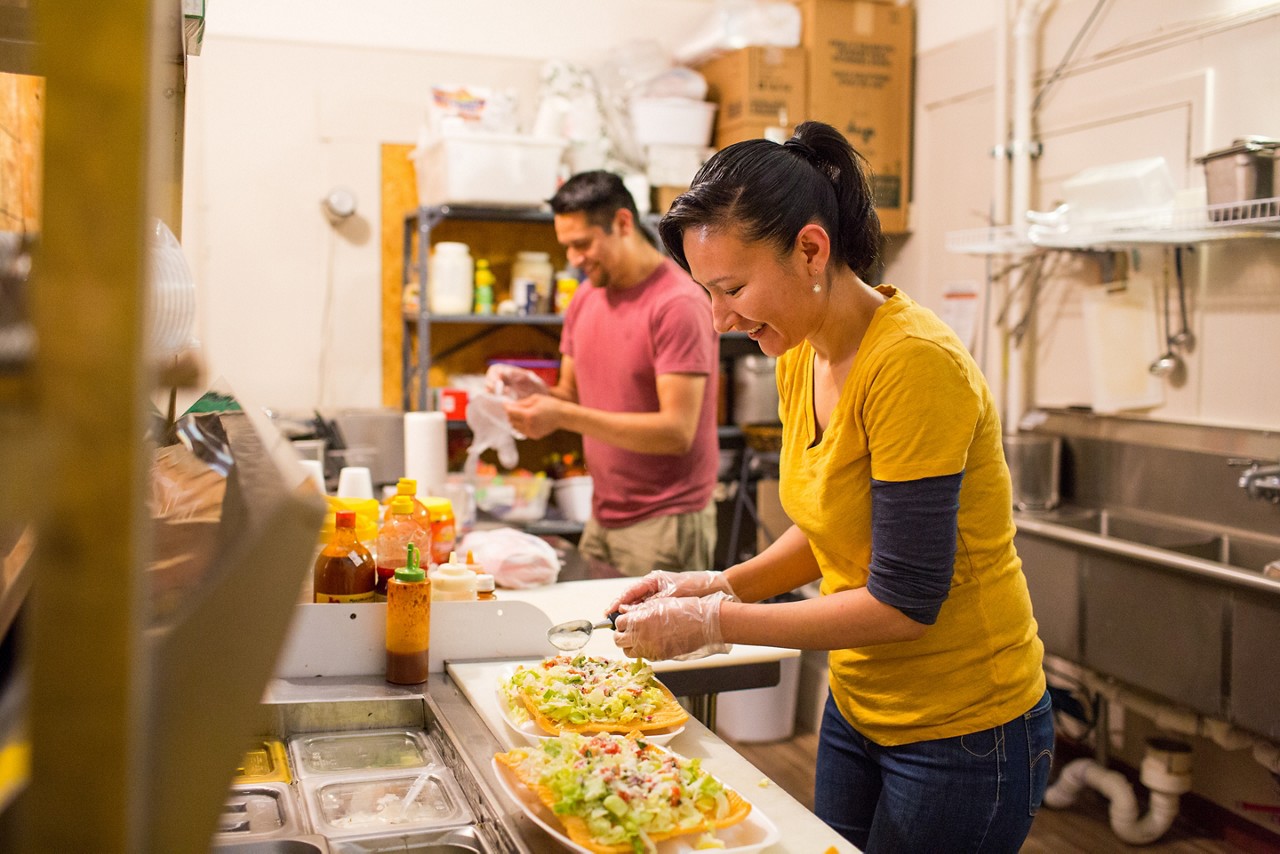 A woman and man preparing food at a store.