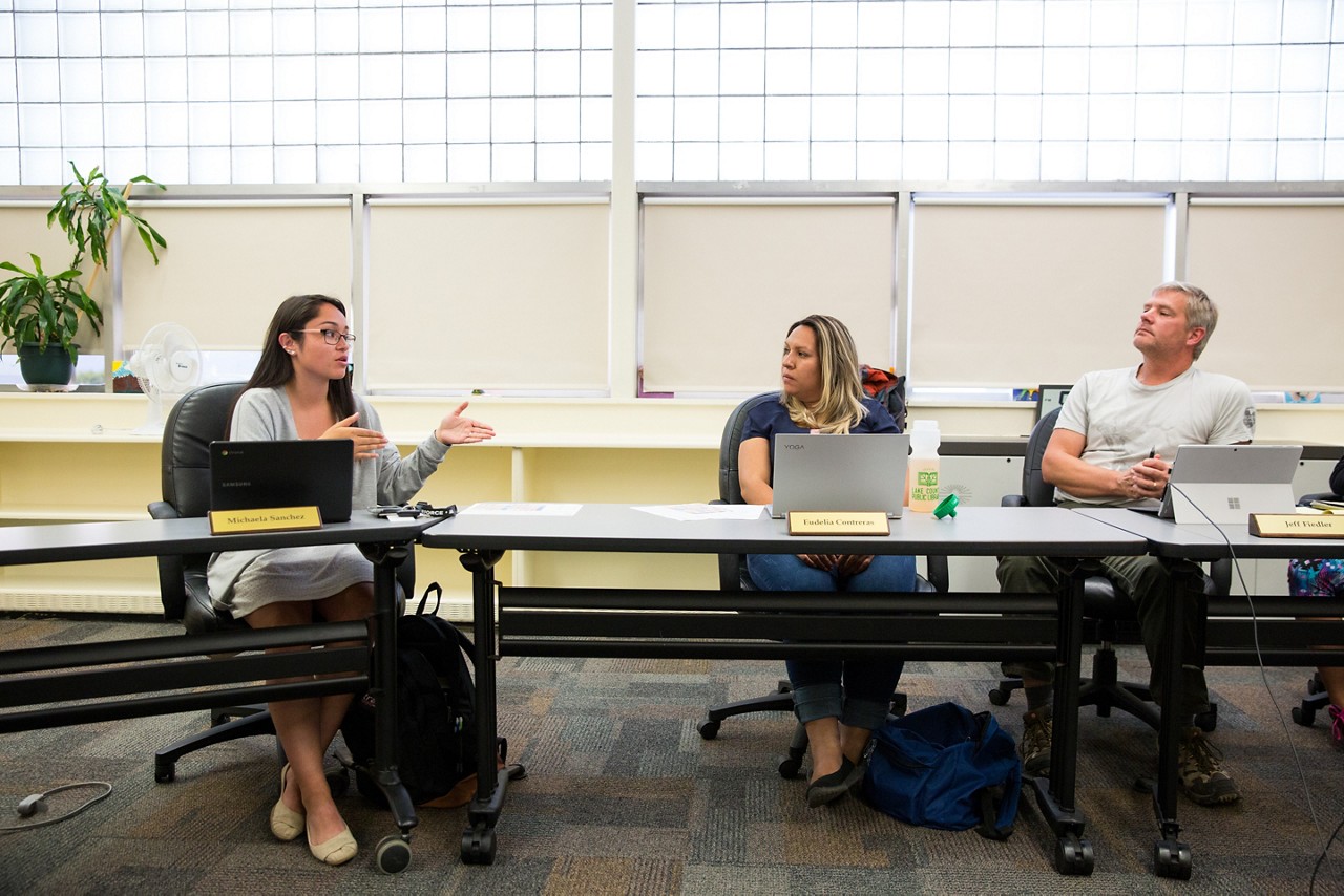 A high school student meeting with two school educators at a long table.