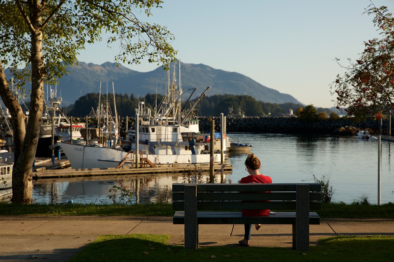 A woman siting on a bench overlooking a harbor.