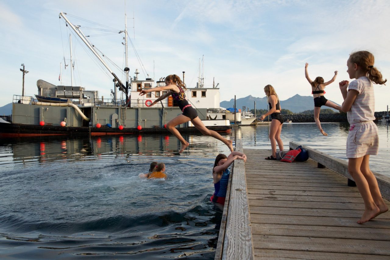 Kids swimming in a harbor off a dock.
