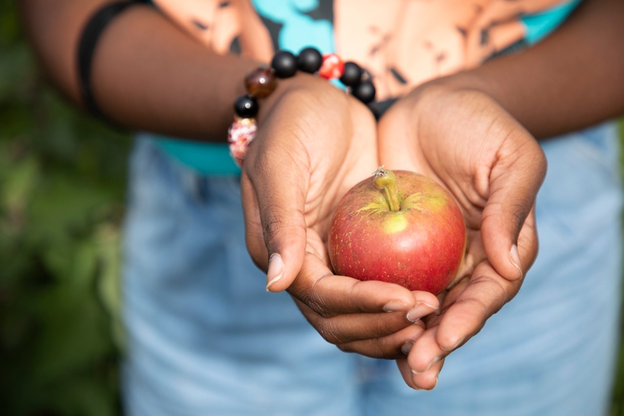 A woman wearing a bracelet holds a small apple.