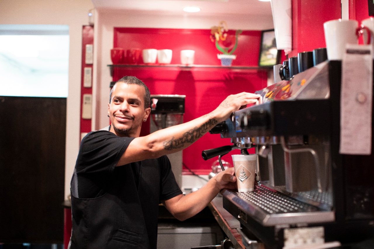 A smiling barista fills a cup with coffee.