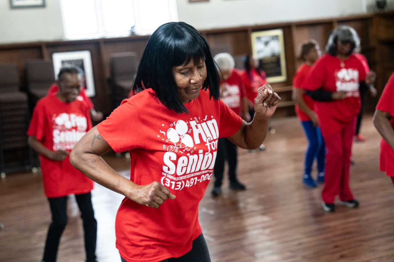 A woman in a red shirt dancing with others dancing in the background. 