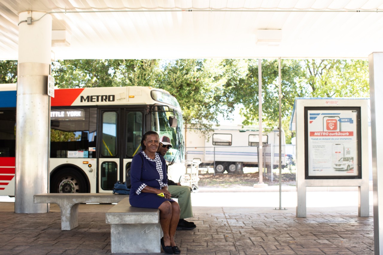A woman and man sit on a bunch at a bus stop.