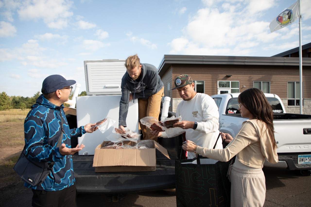 Four people standing at the back of a truck pulling fish out of a box. 