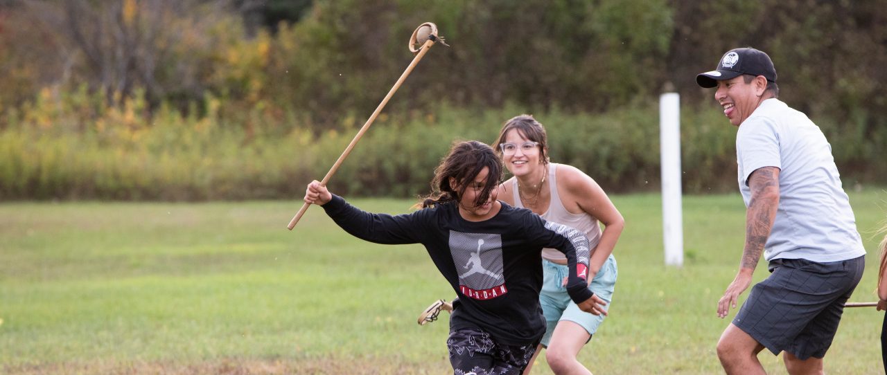 A group of people running on a field with large sticks in their hands.