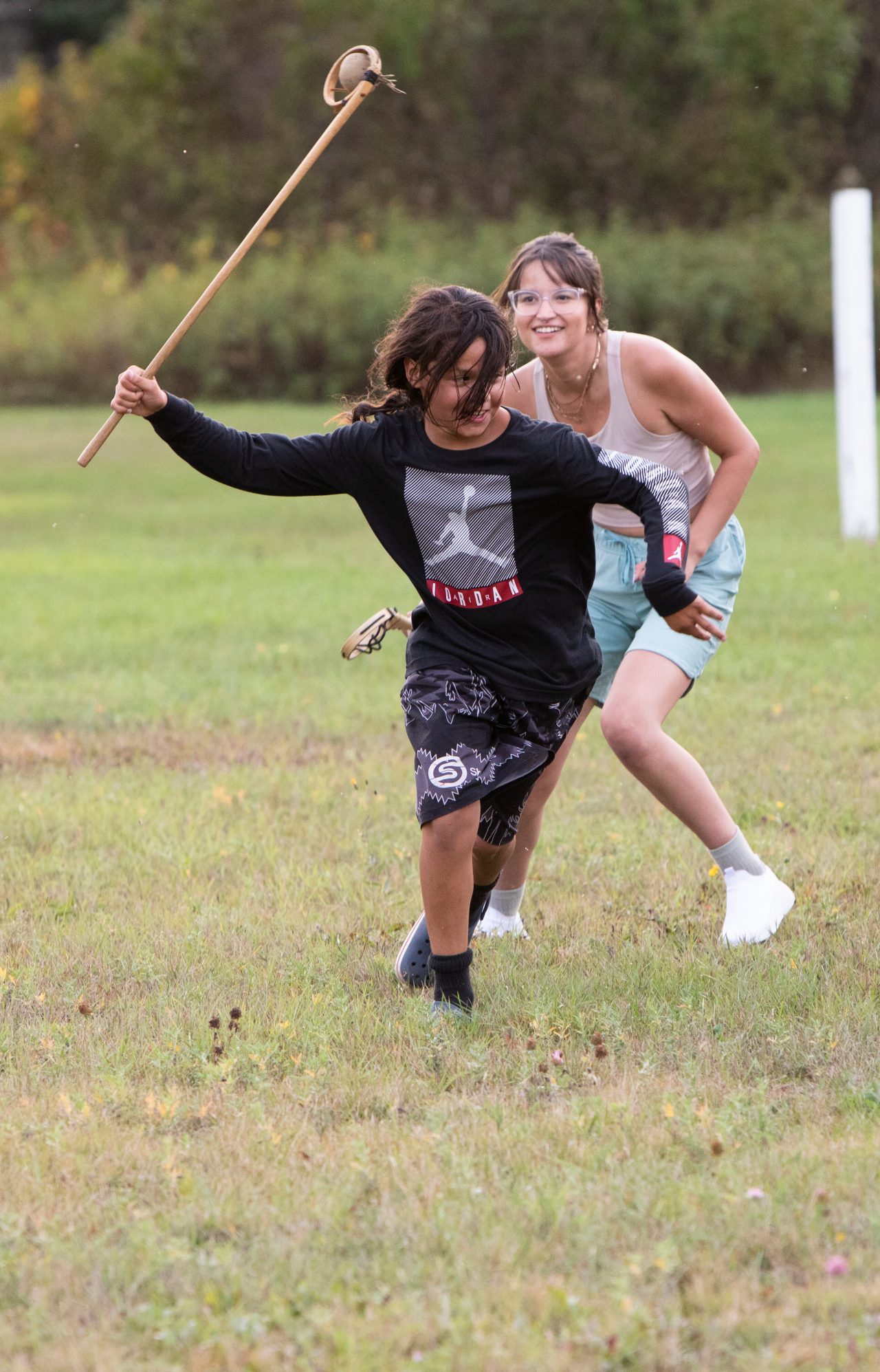 A group of people running on a field with large sticks in their hands.