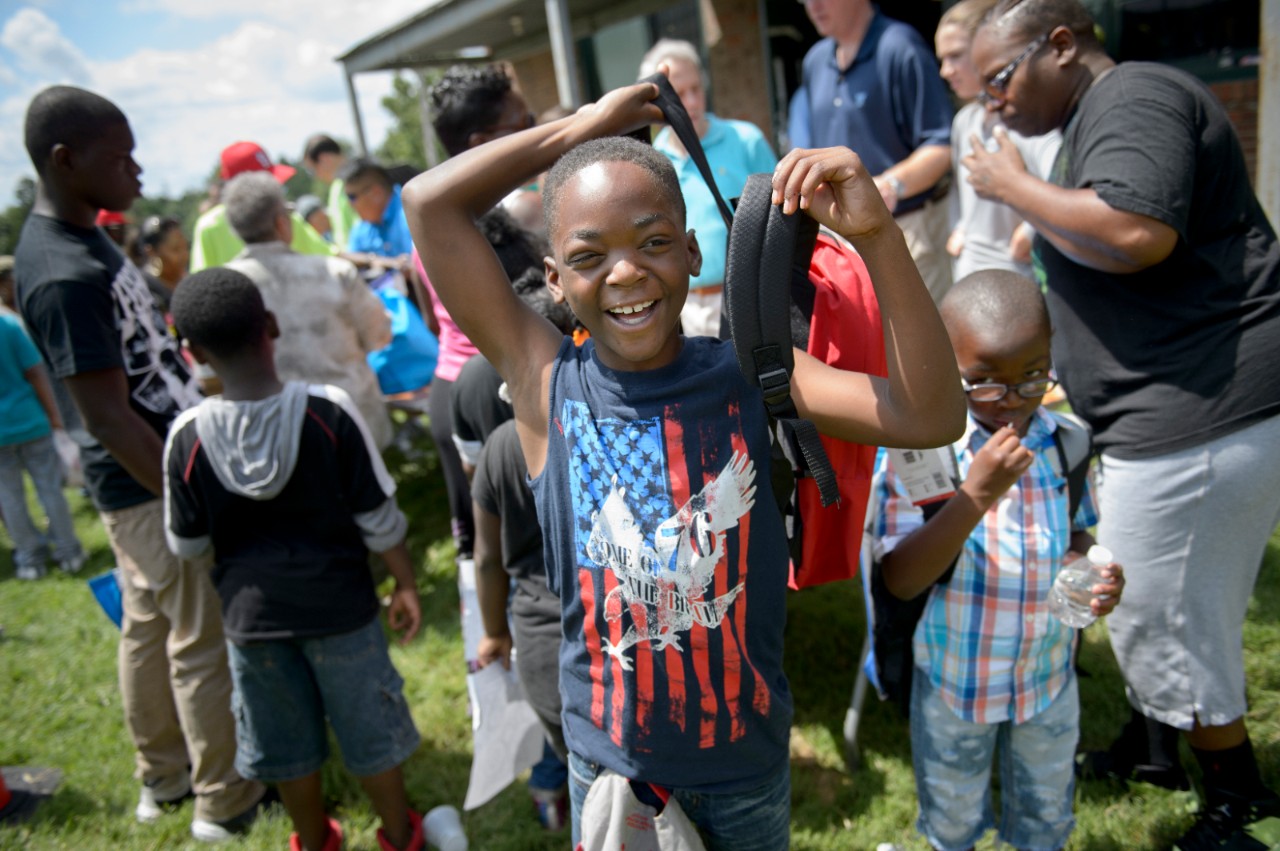 A young boy smiling after receiving a new backpack during a community event.