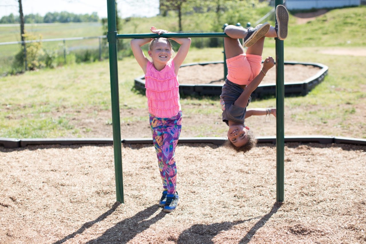 Two young girls playing on playground equipment.