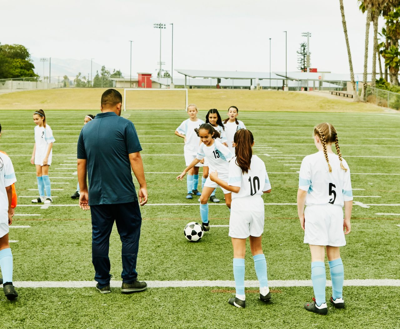 Soccer coach watching young female players run drills during practice