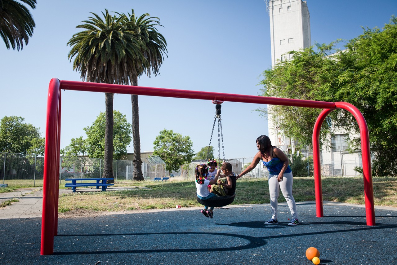 A mother pushing her children on a tire swing in a city park.