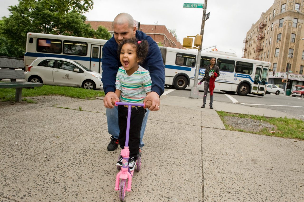 A father and daughter ride on a scooter together.