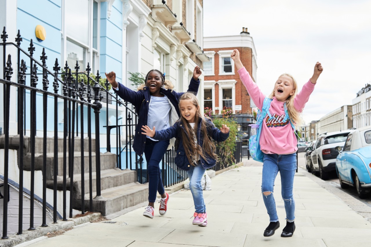 Super happy kids running away after finishing school for winter break with hands up.