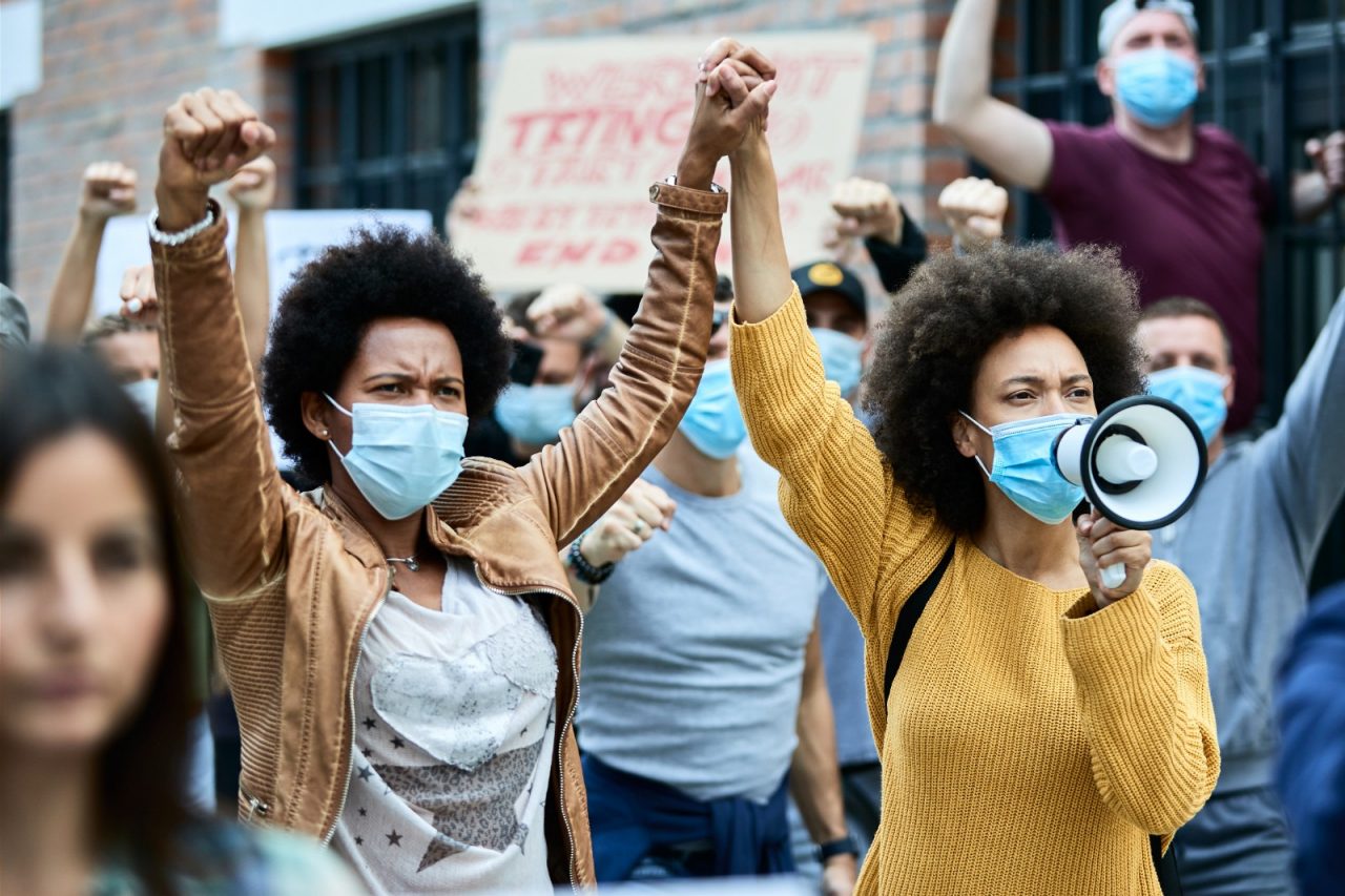 African American woman wearing protective face masks and holding hands while participating in demonstrations for human rights on the streets.