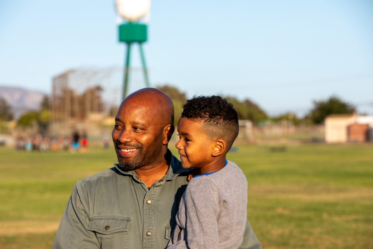 RWJF Culture of Health Prize 2019 - Gonzales, CA. Calvin Dawson (dad) and CJ Dawson (age 4 - and his son) attend Calvin's daughter's cheer leading practice. Calvin works in I.T. and previously lived in Sacramento. They moved to Gonzales to be closer to family.