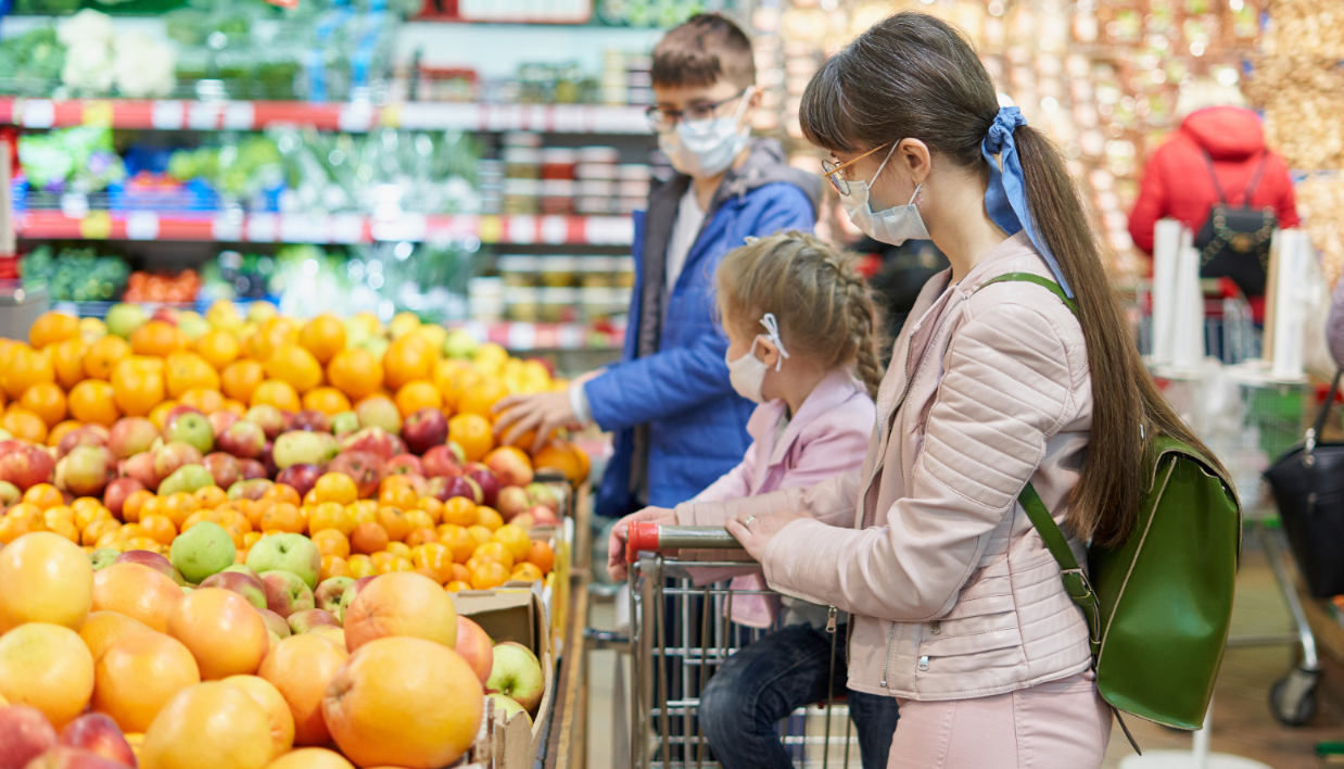 Mom with children in protective masks choose fruits to buy in the store.