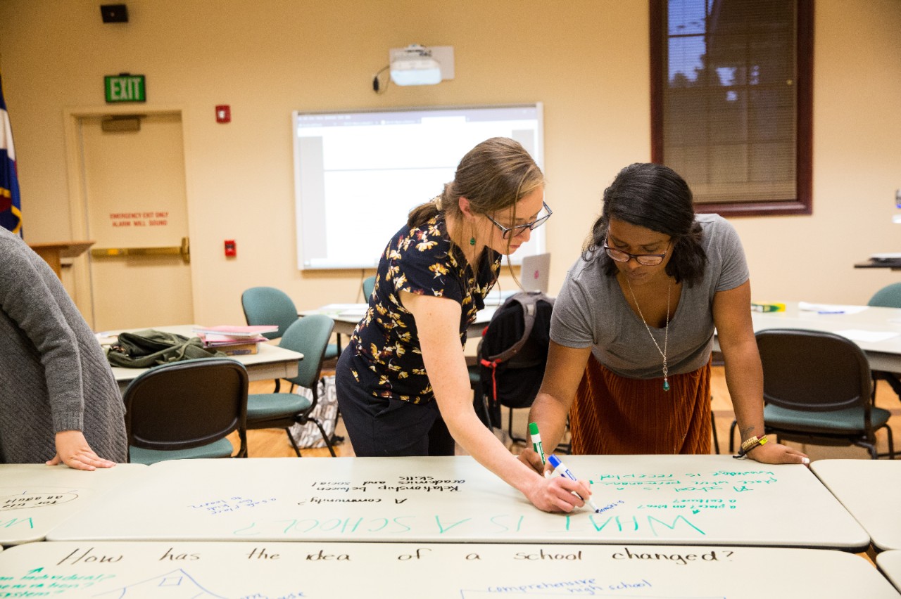Two women write on a whiteboard in a conference room.