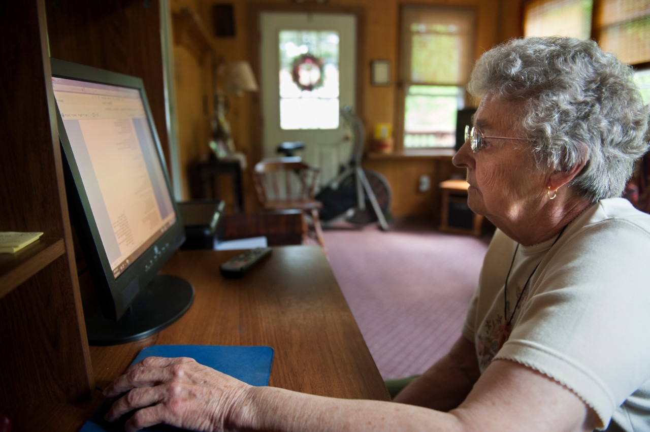 An older woman uses a laptop at home.