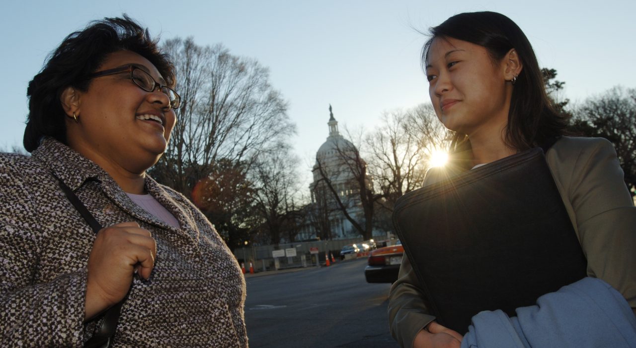 Professional women talk outdoors in Washington, DC, with the Capitol Building in the background.