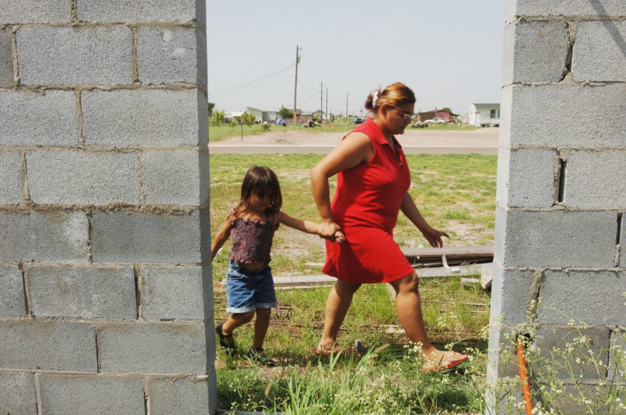 A mother and her daughter walk behind a partially built house.