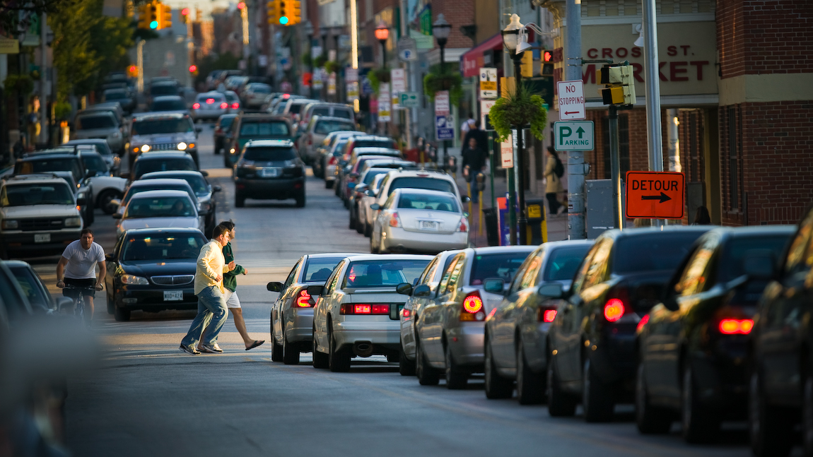 Streets with parked and moving cars and buildings in  Baltimore, Maryland.