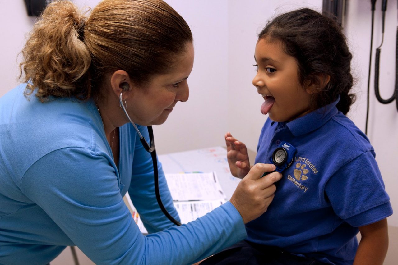 A medical professional listens to a girl's heart using a stethoscope.