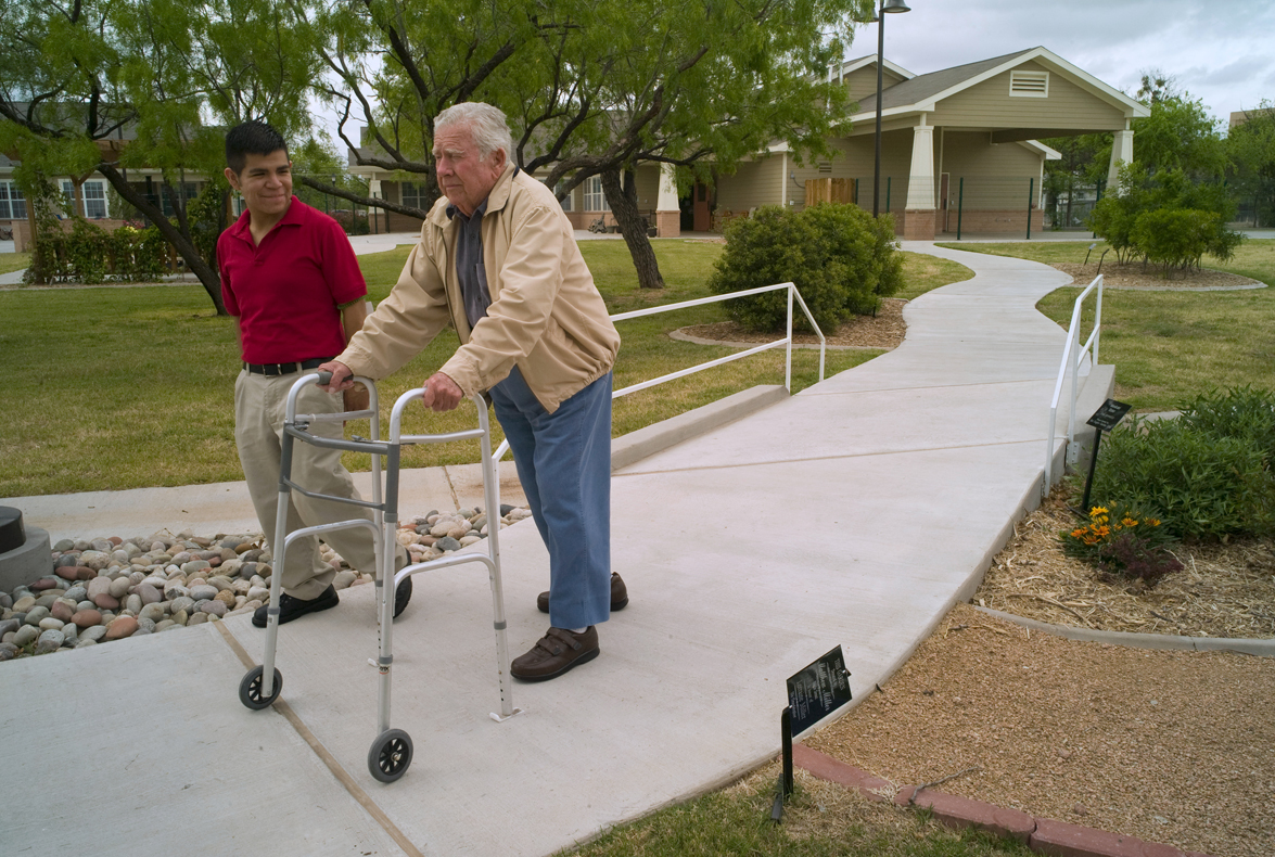Elderly resident of a Green House in San Angelo, Texas, walks outside with his care giver (Shahbaz). Resident using a walker.