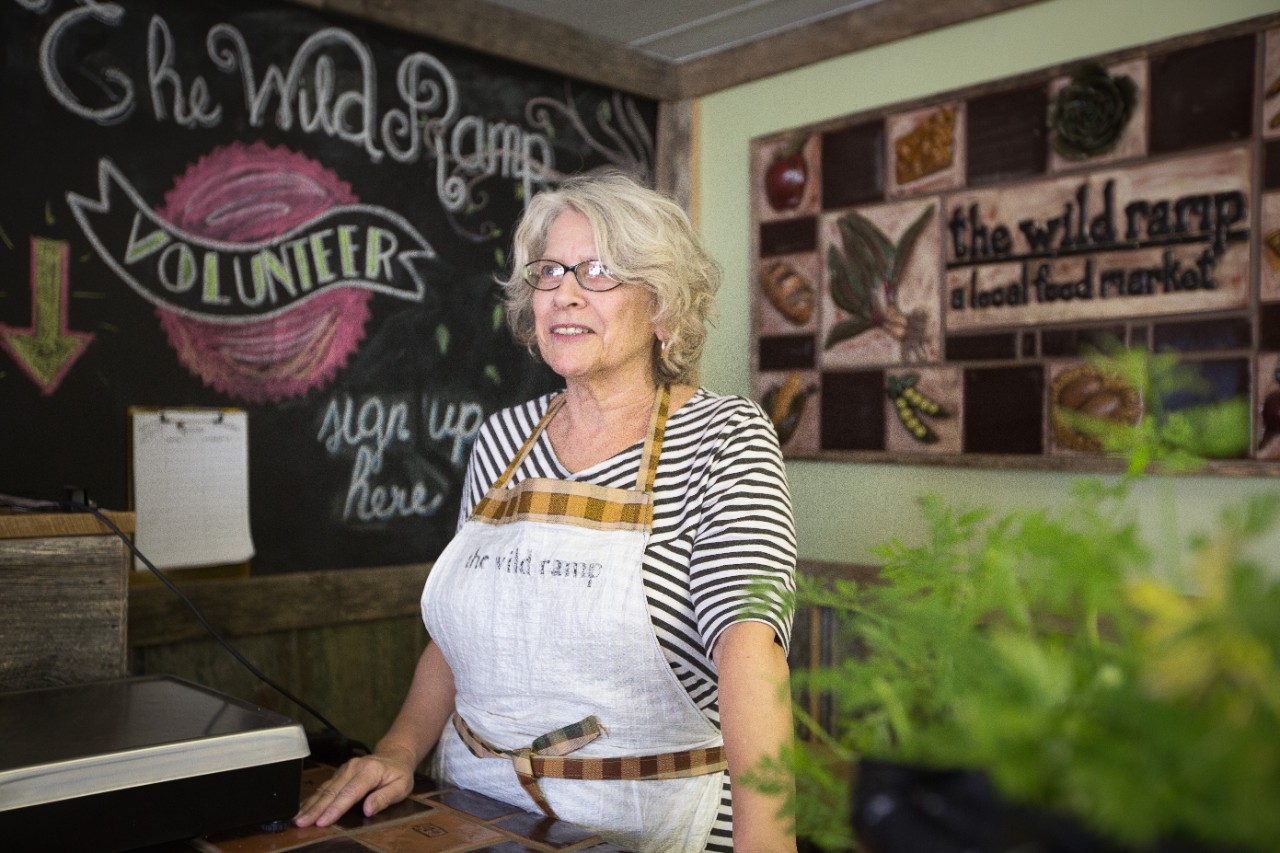 A woman stands behind a counter wearing an apron.