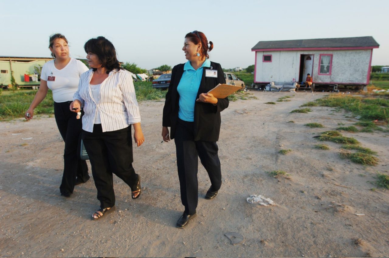 Three women walking outside a home with clipboards.