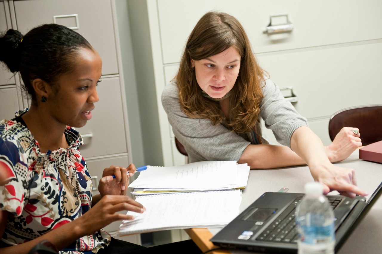 A woman works with a teenager using a laptop in an office.