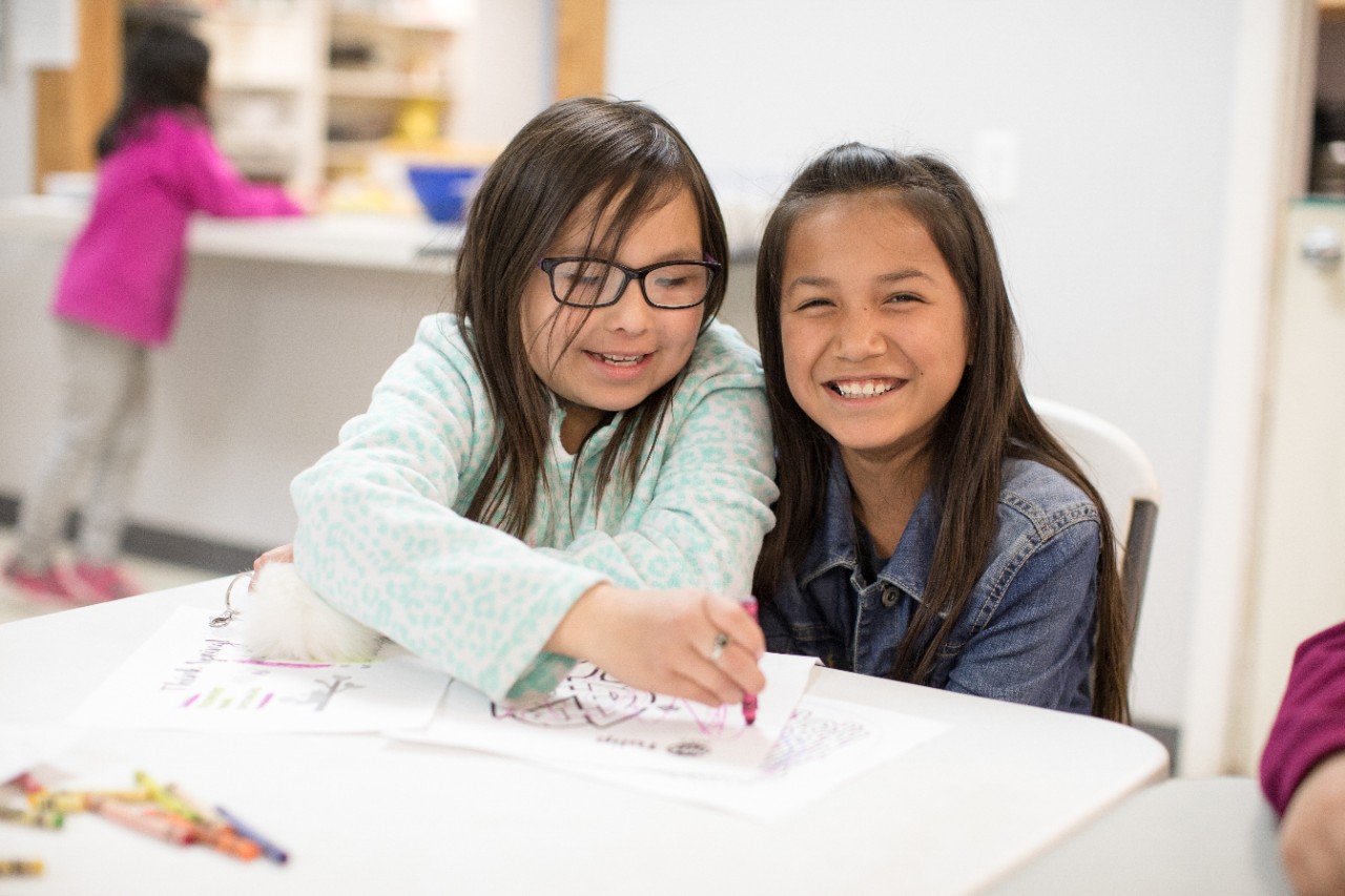 Two girls smiling, drawing with crayons.