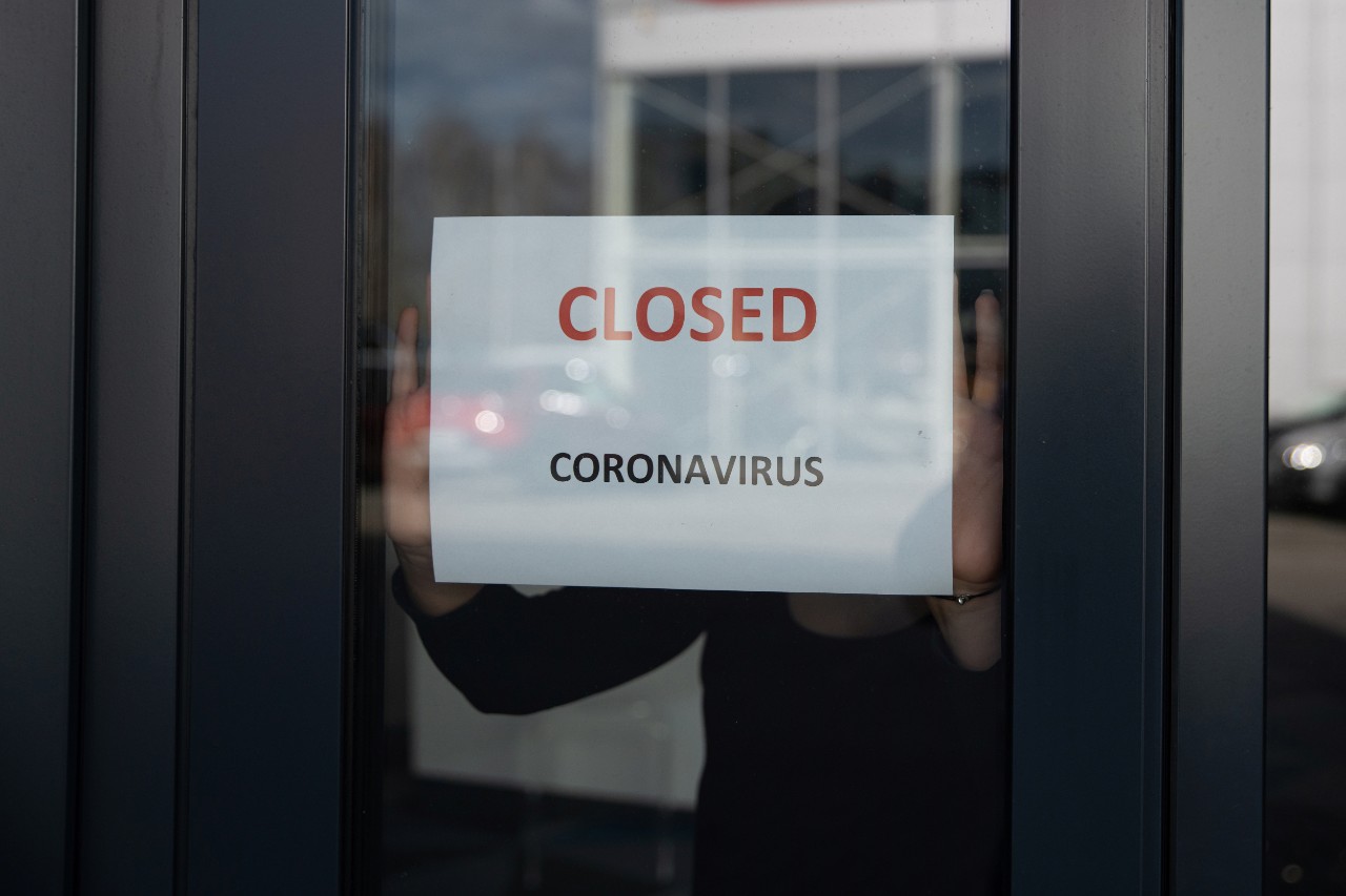 A woman hangs a card with information about the store closing on a shop window