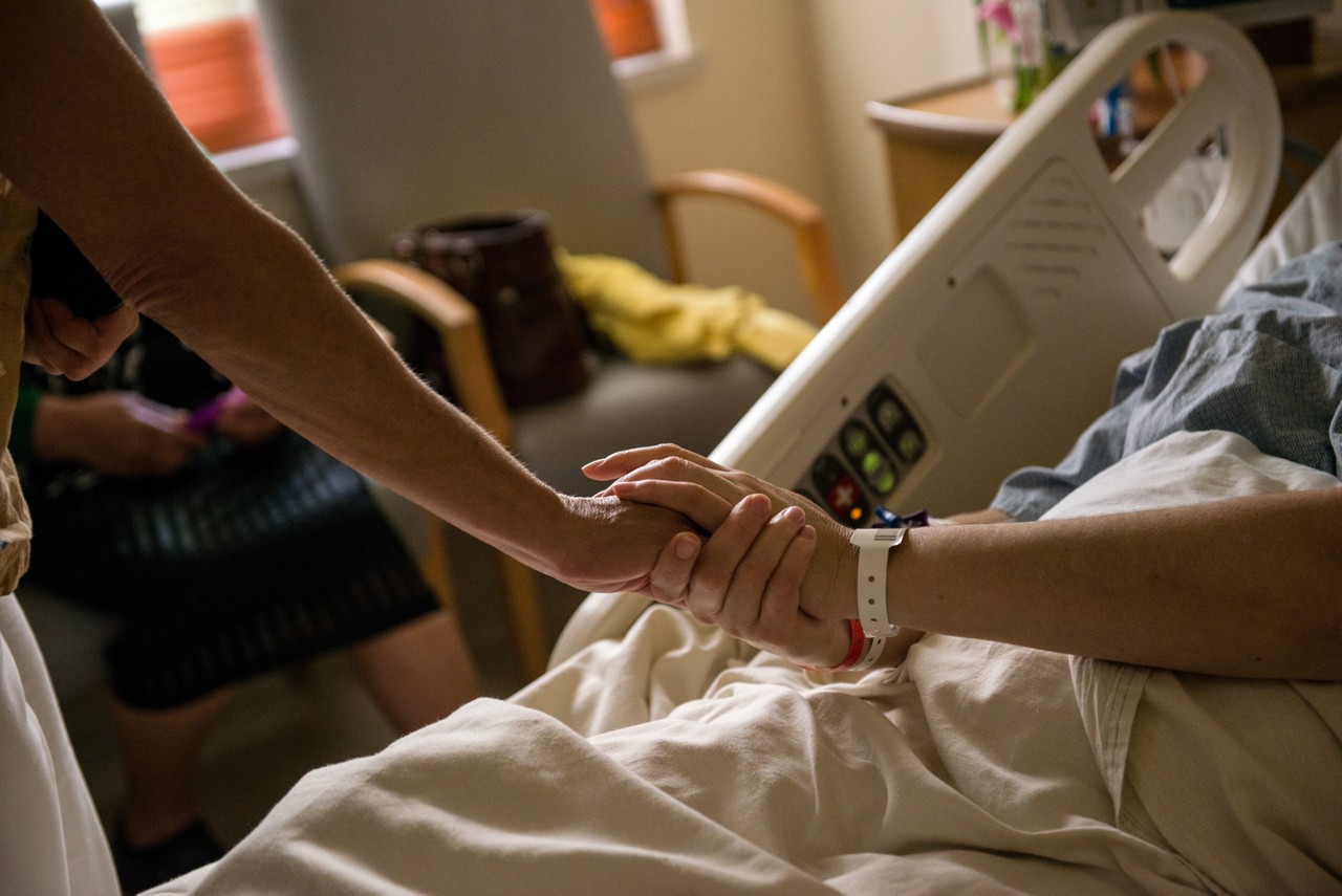Caretaker holding patient's hand from hospital bed. Healh care workers with the St. Josephs Queen of the Valley Hospital in Napa, California care for in and out patients in the hospital and in their homes.
(Credit: Lynsey Addario)