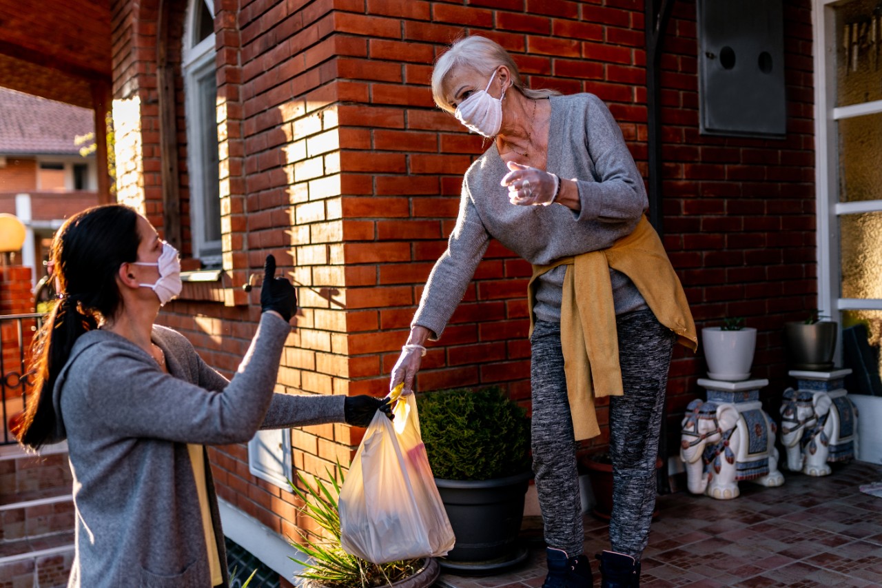 A woman delivers a bag of food to another woman. Ordered by Joan Barlow from iStock.