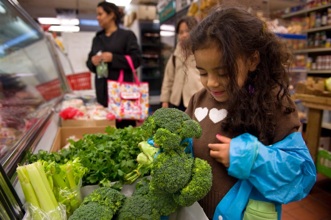 A girl looking at broccoli in a store.