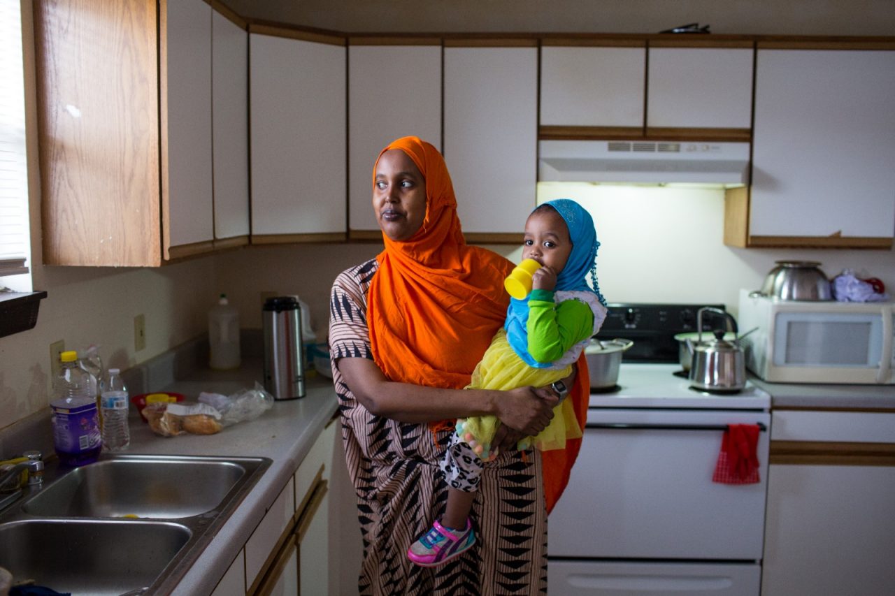 Woman holding her child stands in a kitchen.