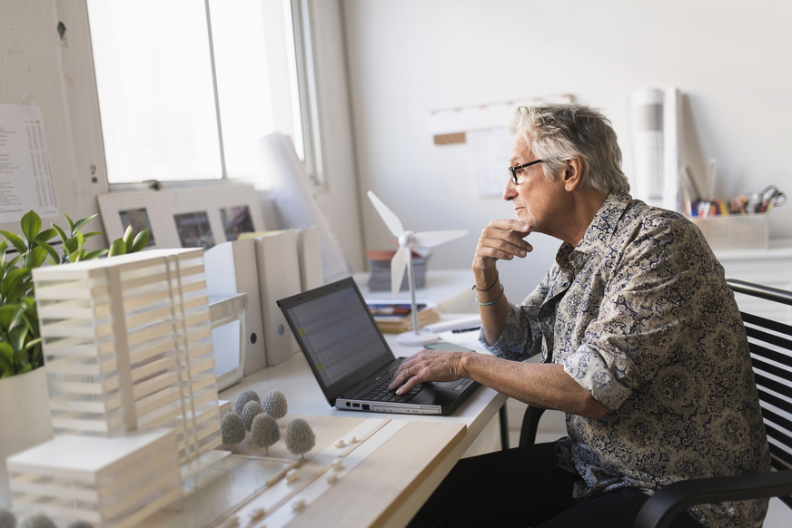 Older man working in office on laptop.