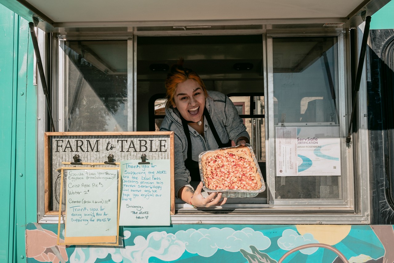 A woman operating a mobile kitchen bus at a farmers market.