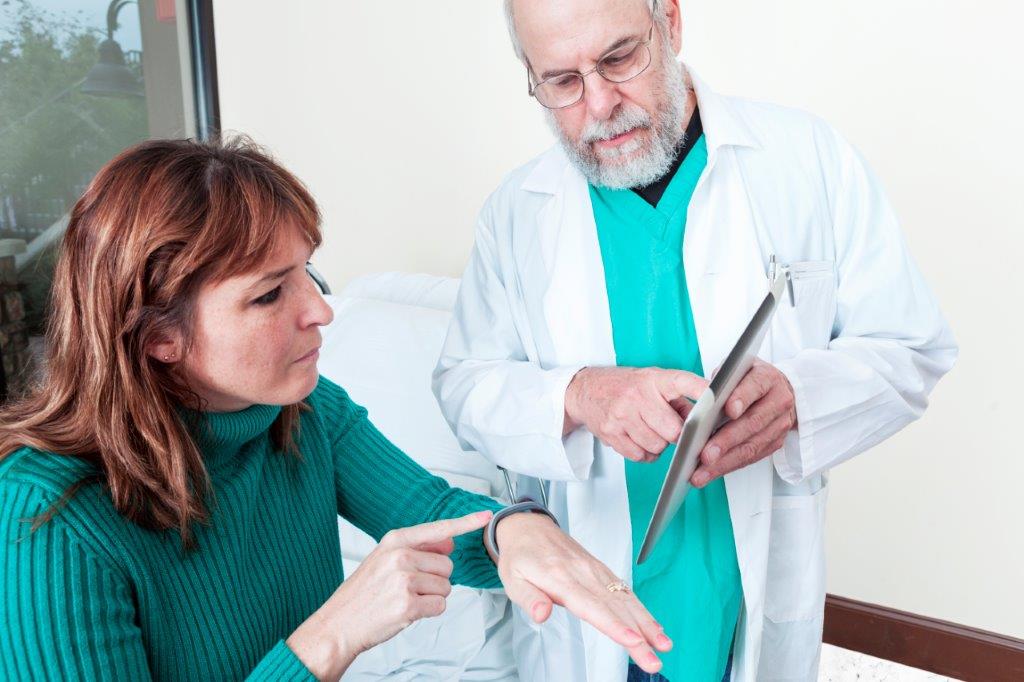 
Older male medical professional showing female middle-aged woman how to use health monitoring on tablet and smart watch.
