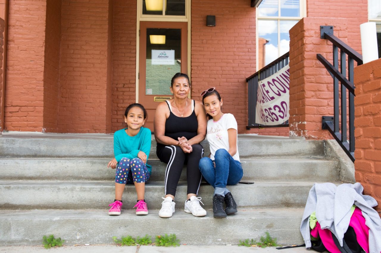A grandmother sits with her granddaughters on their apartment building steps.