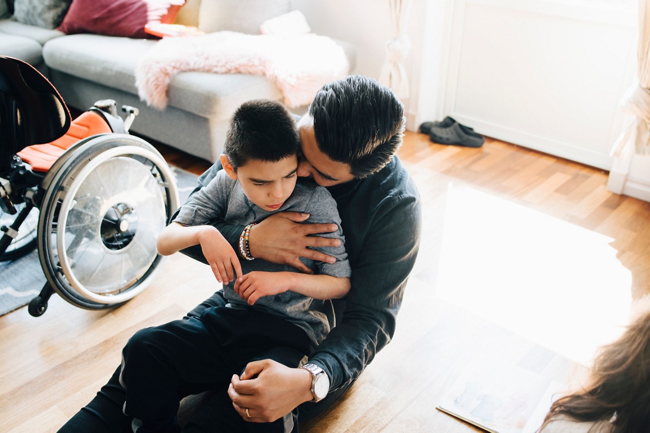 A man holds and hugs a disabled boy.