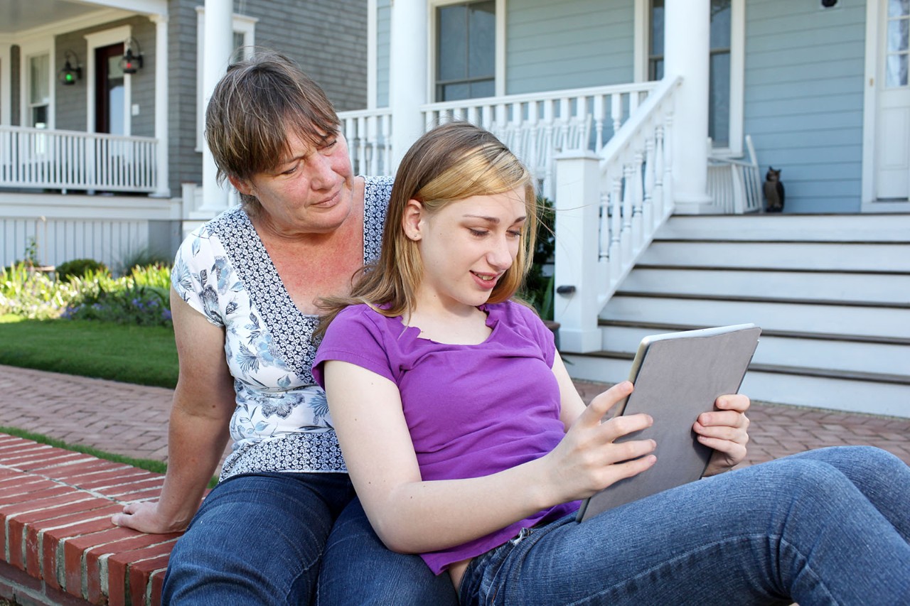 Mother watches over her teenage daughter as she uses a tablet.