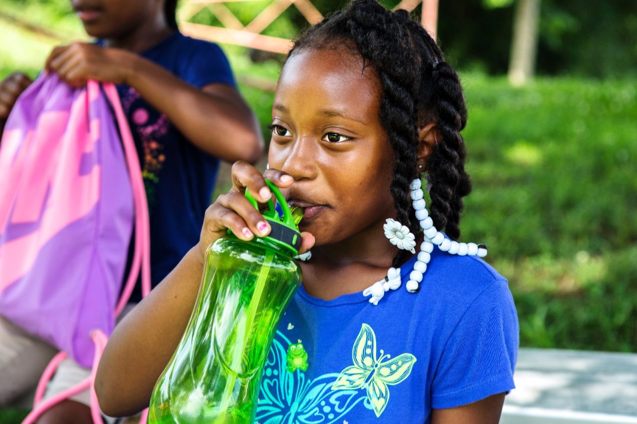 A young girl drinking from a water bottle after a sporting event.
