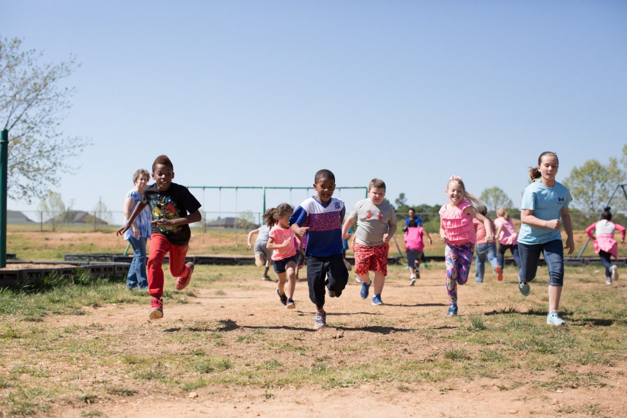 A group of young children running in a playground field.