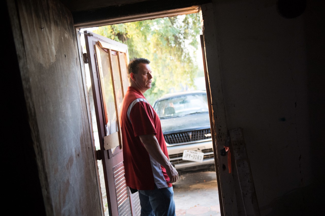 A man stands in the doorway of a garage with a truck parked in the driveway.